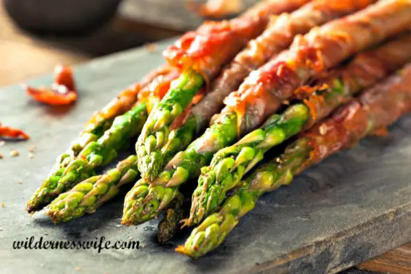 Our Bacon Wrapped Asparagus Recipe on a cutting board showing roasted asparagus spears wrapped in crispy bacon.