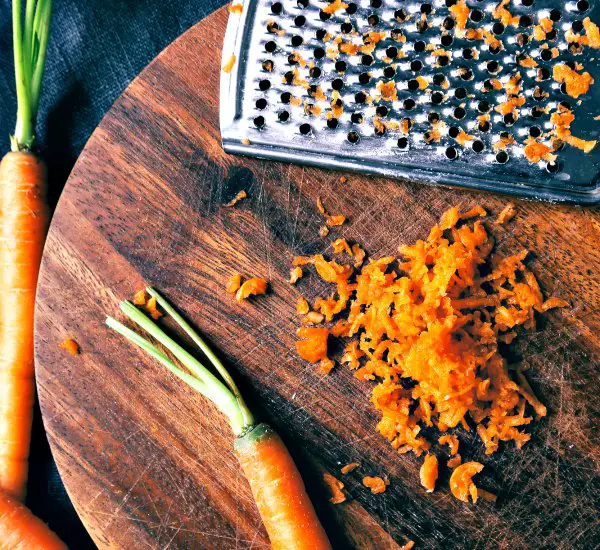 Carrots and grater on wooden cutting board ready to use in basic traditional coleslaw recipe.