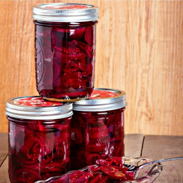 Jars of pickled beet sitting on a counter with a dish of pickled beets in front of them. 