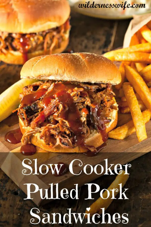 Juicy slow cooker pulled pork sandwich sitting on wooden cutting board with a side of french fries