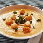 A steaming bowl of Butternut Squash soup with crispy croutons.