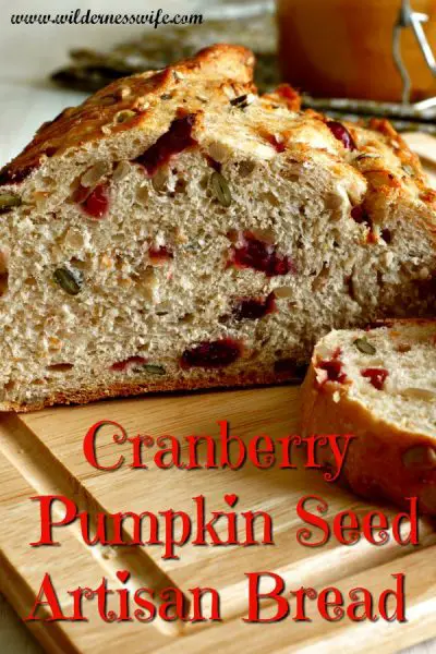 Loaf of Cranberry Pumpkin Seed Artisan Yeast Bread sliced on a wooden cutting board.