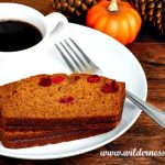 Pumpkin cranberry bread on a white plate with a cup of coffee and a mini pumpkin
