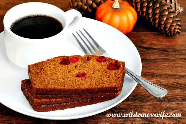 Pumpkin cranberry bread on a white plate with a cup of coffee and a mini pumpkin