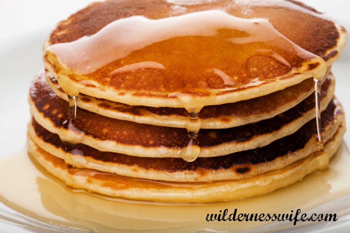 Stack of pancakes drenched in syrup on a white plate