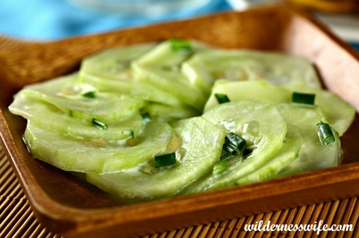 cucumber salad garnished with chopped chives in a wooden bowl 0n a brown cloth placemat