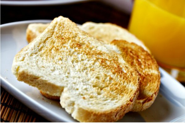 3 slices of homemade white bread on a plate next to a glass of orange juice