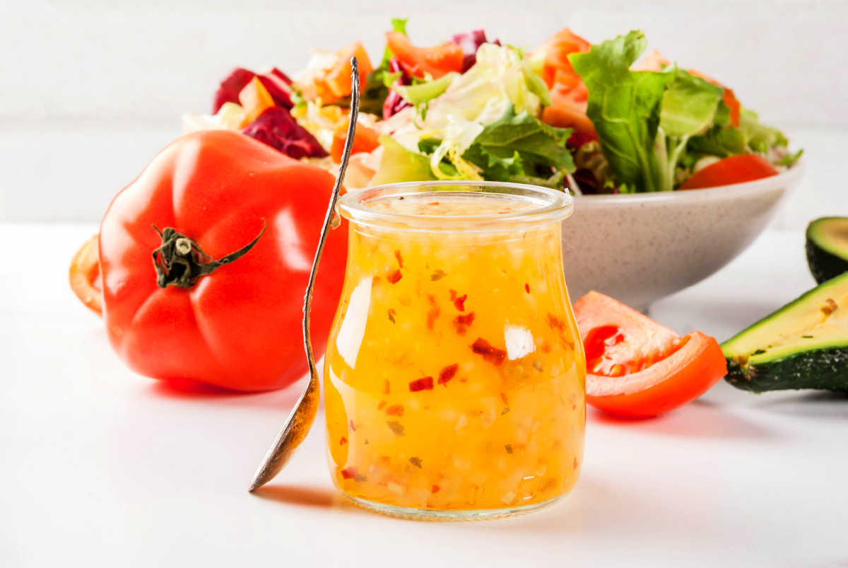 Glass jar full of homemade Italian Salad Dressing in front of a bowl of garden salad and a ripe tomato