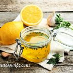 A jar of lemon vinaigrette salad dressing and lemons on a wooden table top