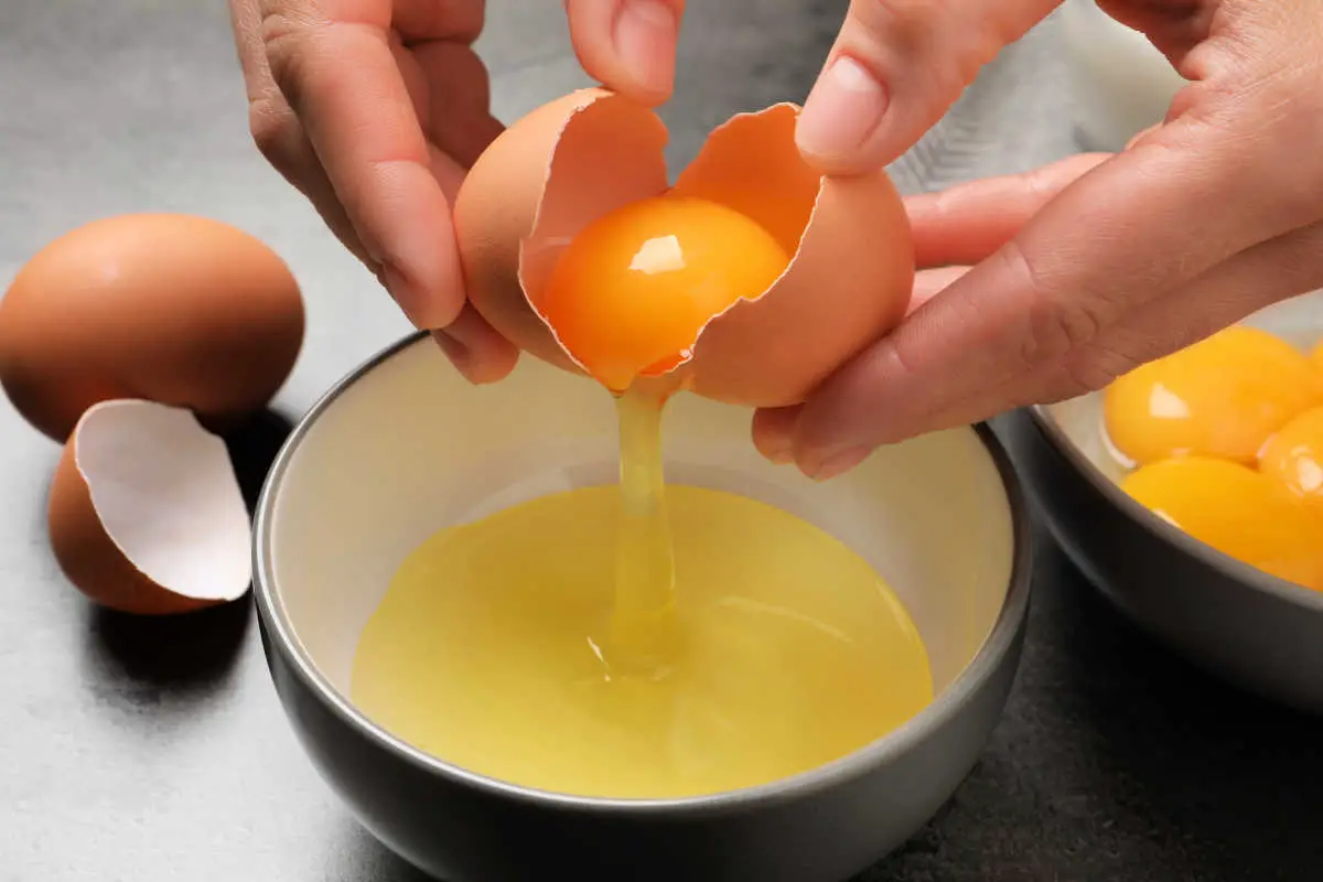 Female hands separating an egg yolk from an egg white into a ceramic bowl