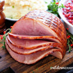 Slow Cooker Bourbon Glazed Spiral Ham on dark wooden cutting board next to white dish filled with whole cranberry sauce