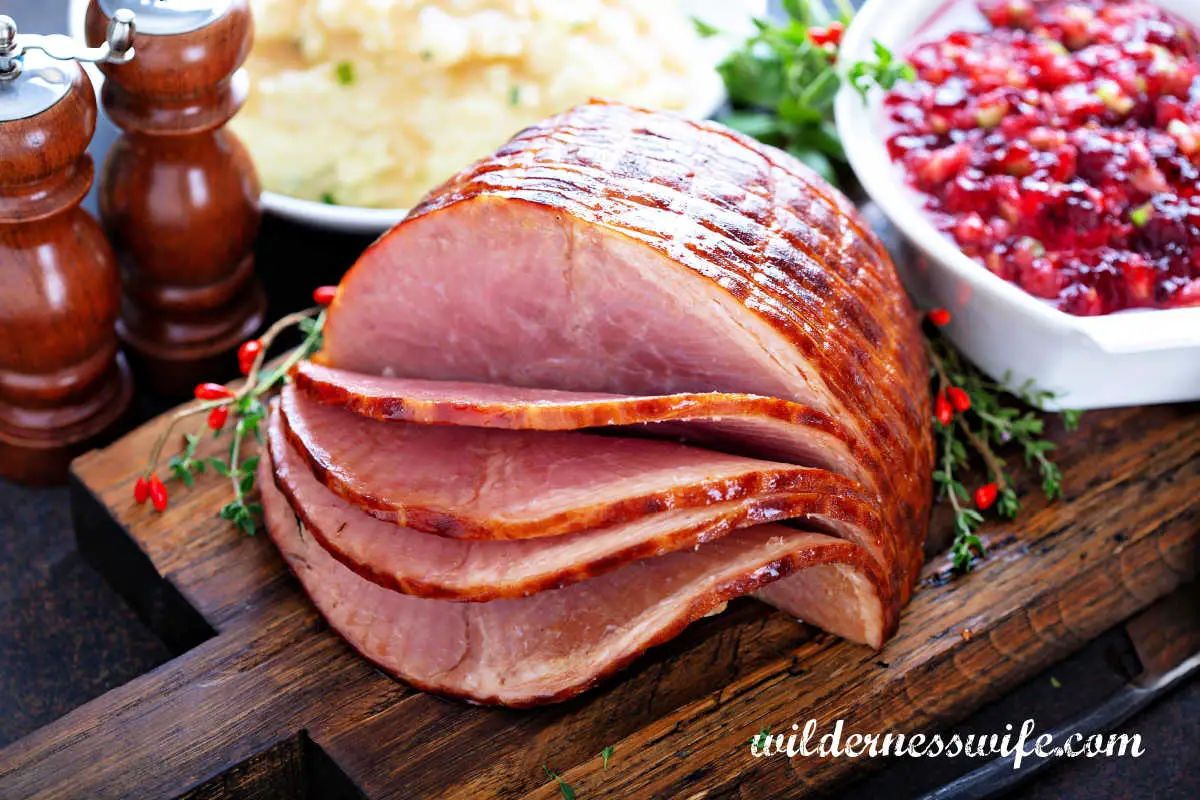 Slow Cooker Bourbon Glazed Spiral Ham on dark wooden cutting board next to white dish filled with whole cranberry sauce