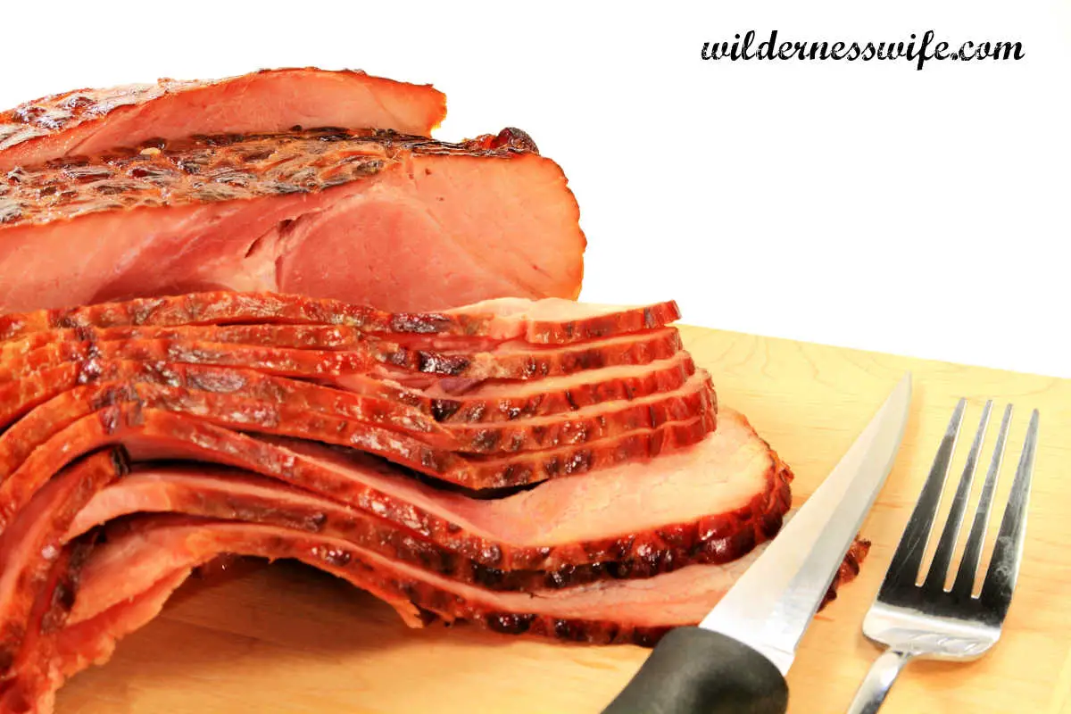 Sliced Crockpot Bourbon Glazed Spiral Ham on Maple Cutting Board with knife and fork next to it