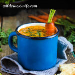 Blue mug sitting ona blue napkin. The mug is holding some steaming hot Slow Cooker Curried Carrot Soup.