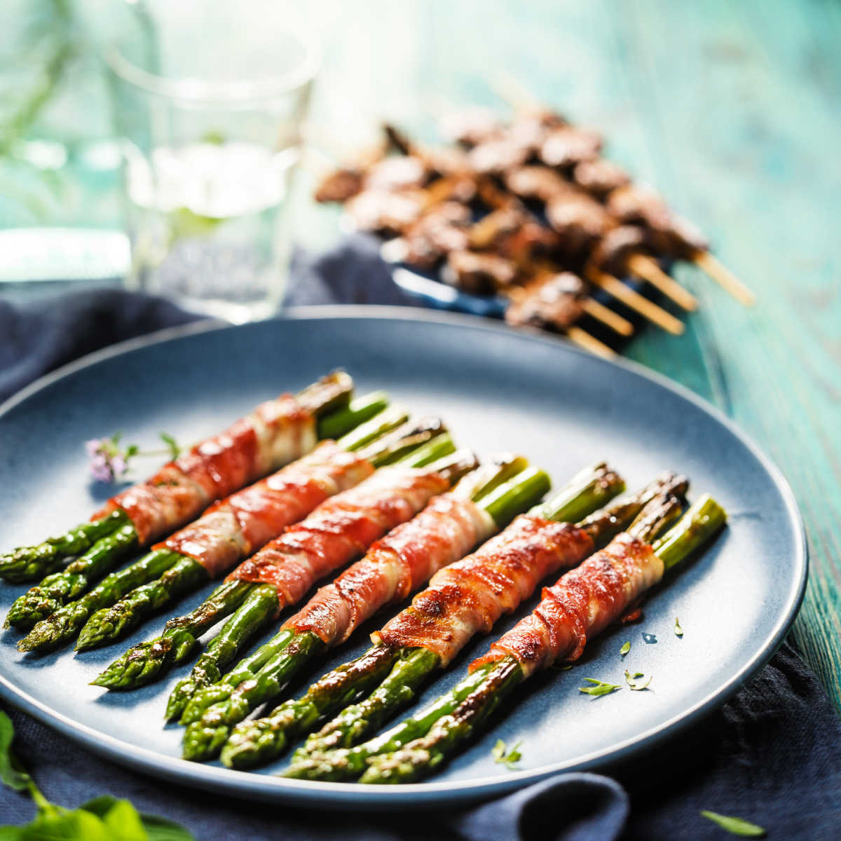 Grey pottery plate holding spears of roasted asparagus wrapped in bacon