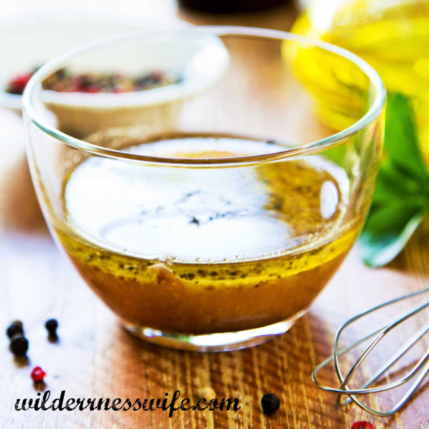 Small glass bowl filled with basic vinaigrette on a bamboo table next to a wire whisk