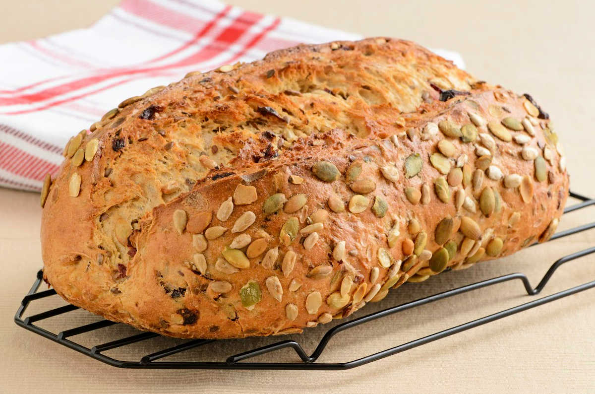 loaf of cranberry pumpkin seed yeast bread on a wire rack on kitchen counter