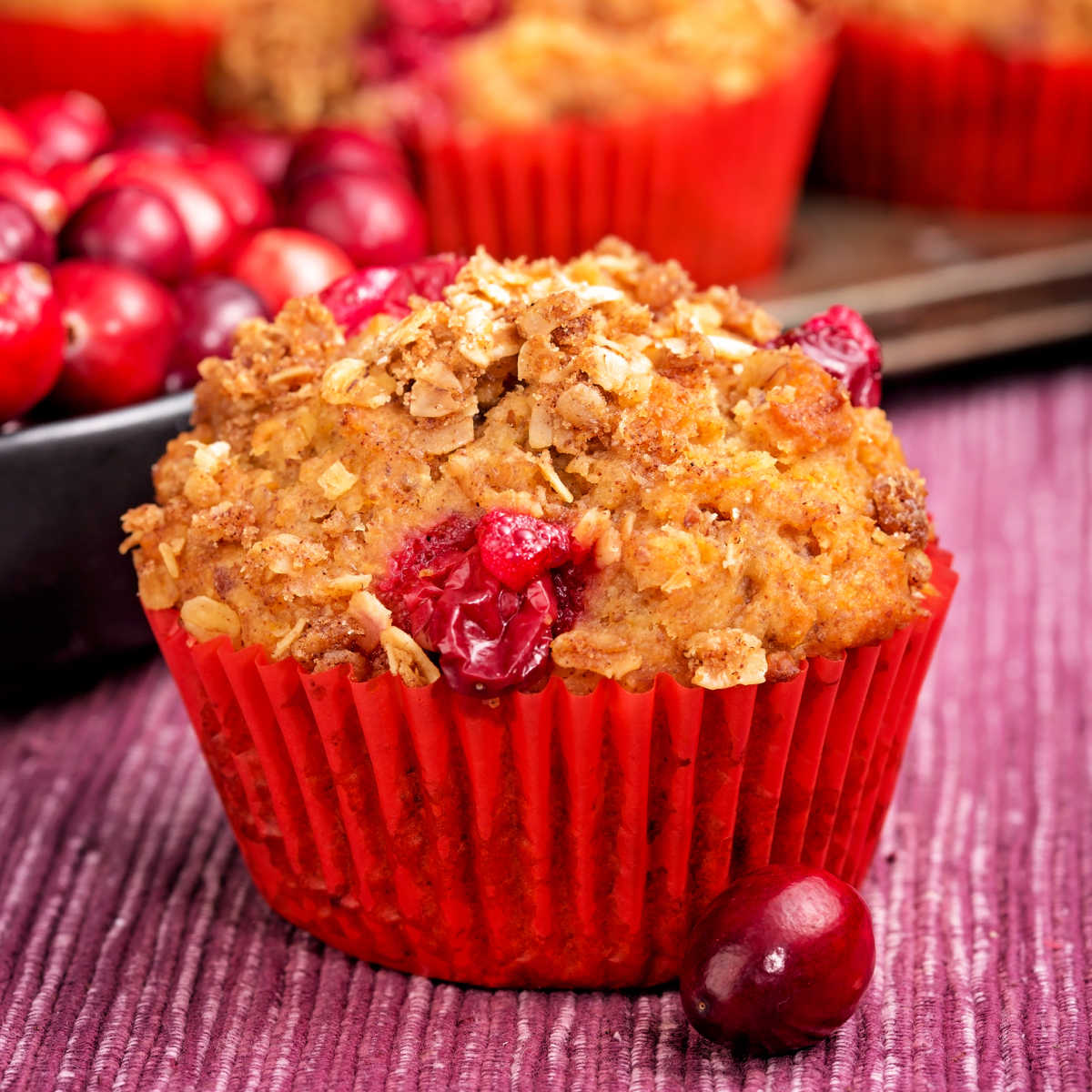 orange cranberry muffin sitting on wood table next to fresh cranberry