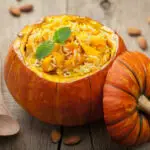 pumpkin bowl full of pumpkin risotto setting on a brown wooden table next to wooden spoon and pumpkin seeds