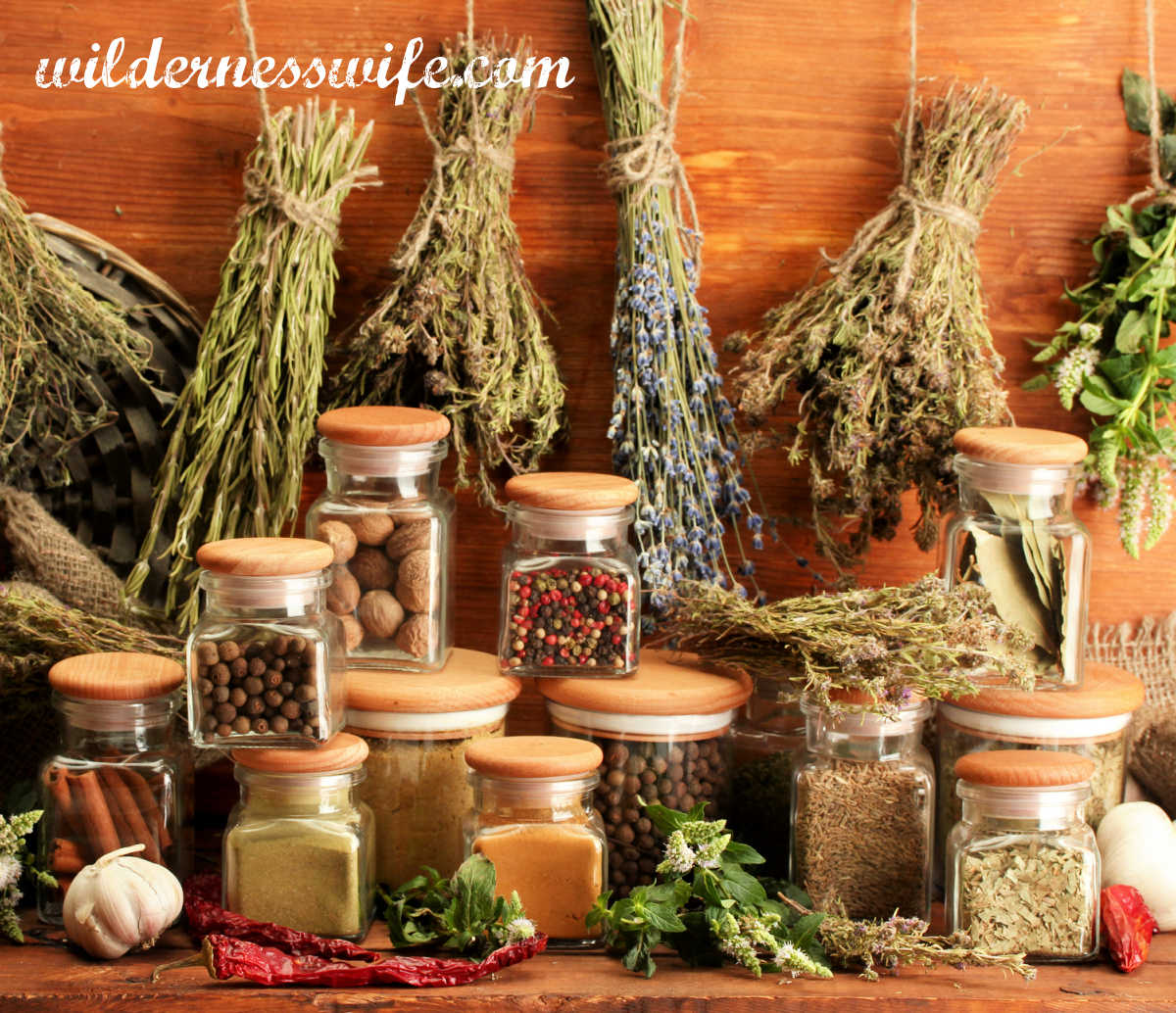 Display of dried herbs and jars of spices that can be used in making vegetable soup. They are displayed against a wood background.