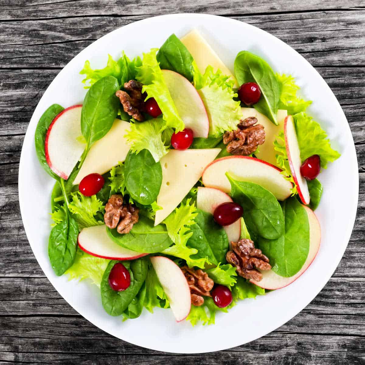 Overhead shot of Apple Spinach Salad on white plate setting on a grey weathered wood table