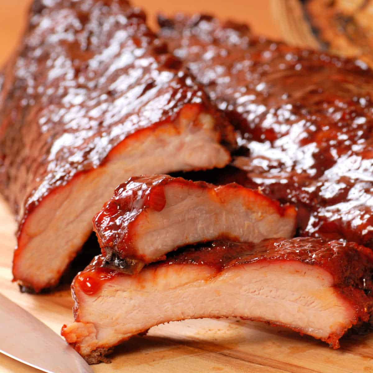 Close-up of pork back ribs dripping with BBQ sauce on wood cutting board