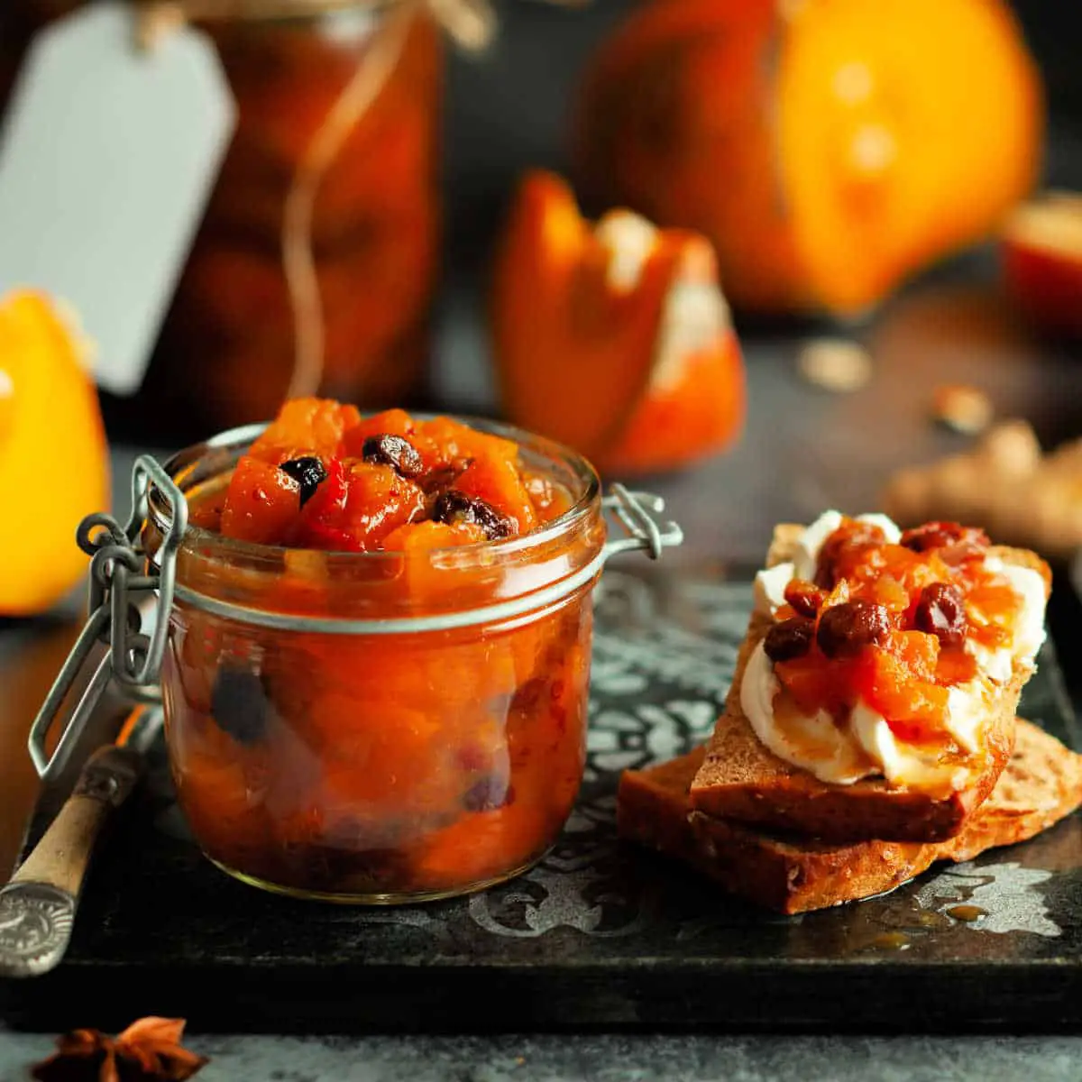 Chunky Pumpkin Chutney in glass canning jar and some spread on toast with cream cheese on dark wood cutting board.