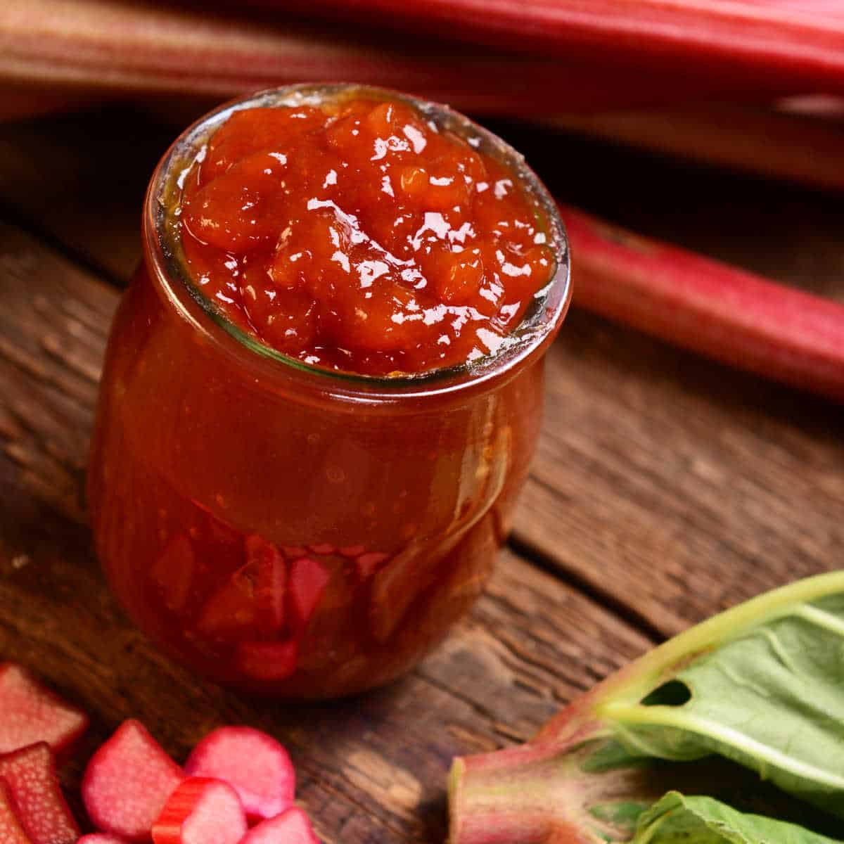 Jar of rhubarb jam sitting on wood table with some cut-up rhubarb