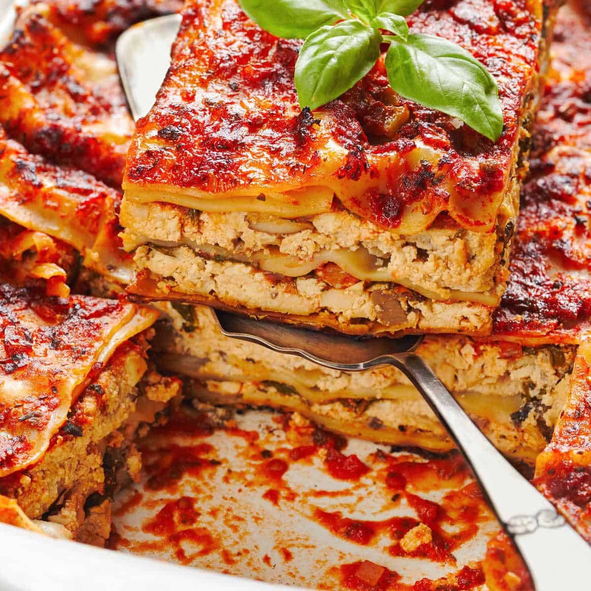 Crockpot vegetable lasagna in white slow cooker liner with one piece in a serving spatula.