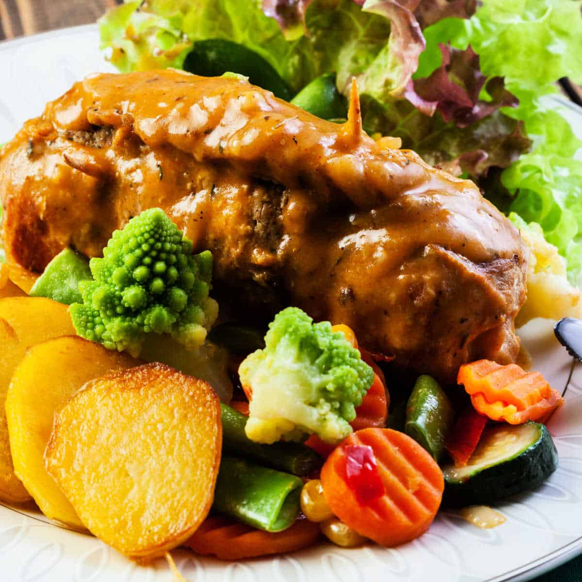 Steak Roulade with celery stuffing on a white plate smothered with gravy along with vegetables and potatoes.