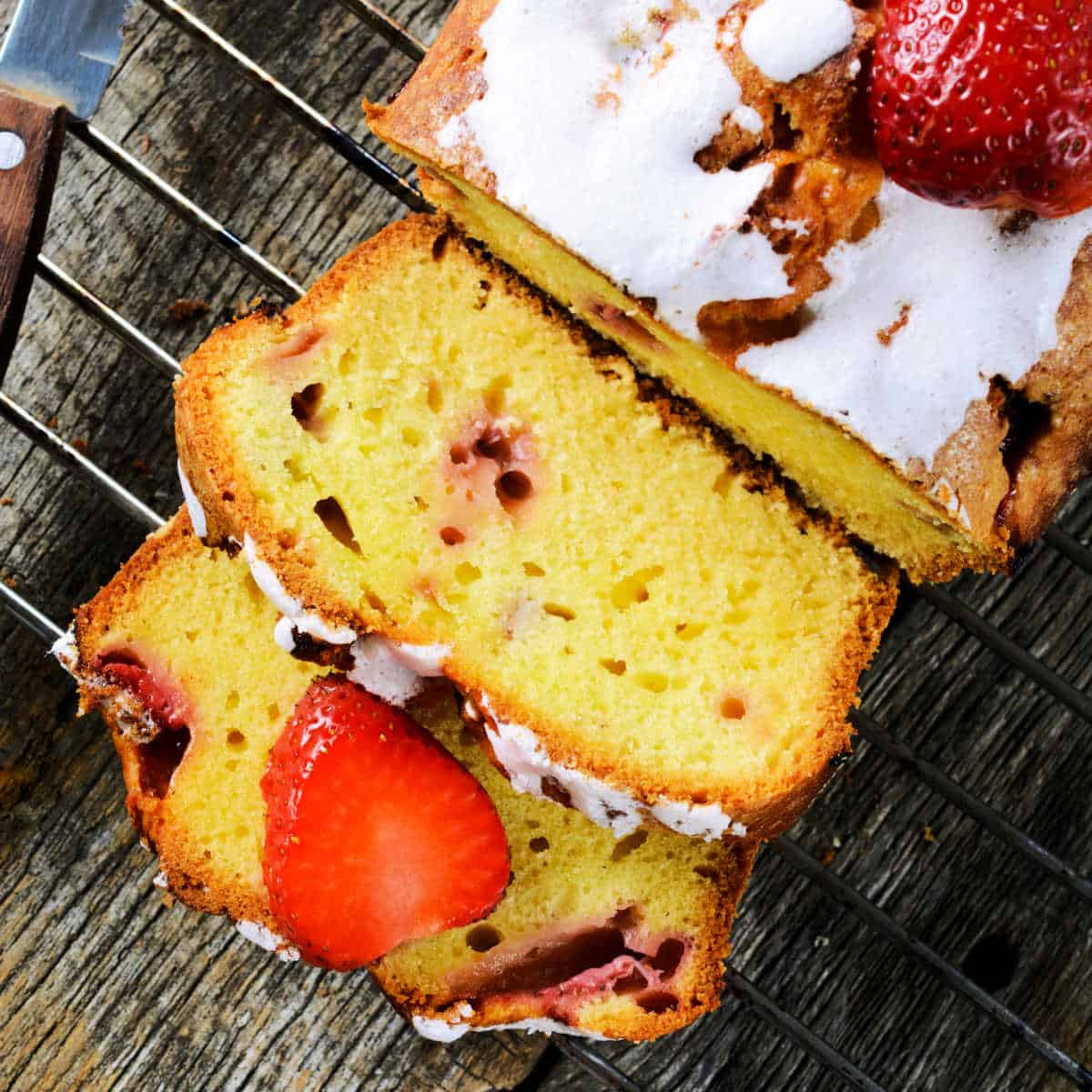 A loaf and slices of strawberry rhubarb bread sitting on a cooling rack on a wood table