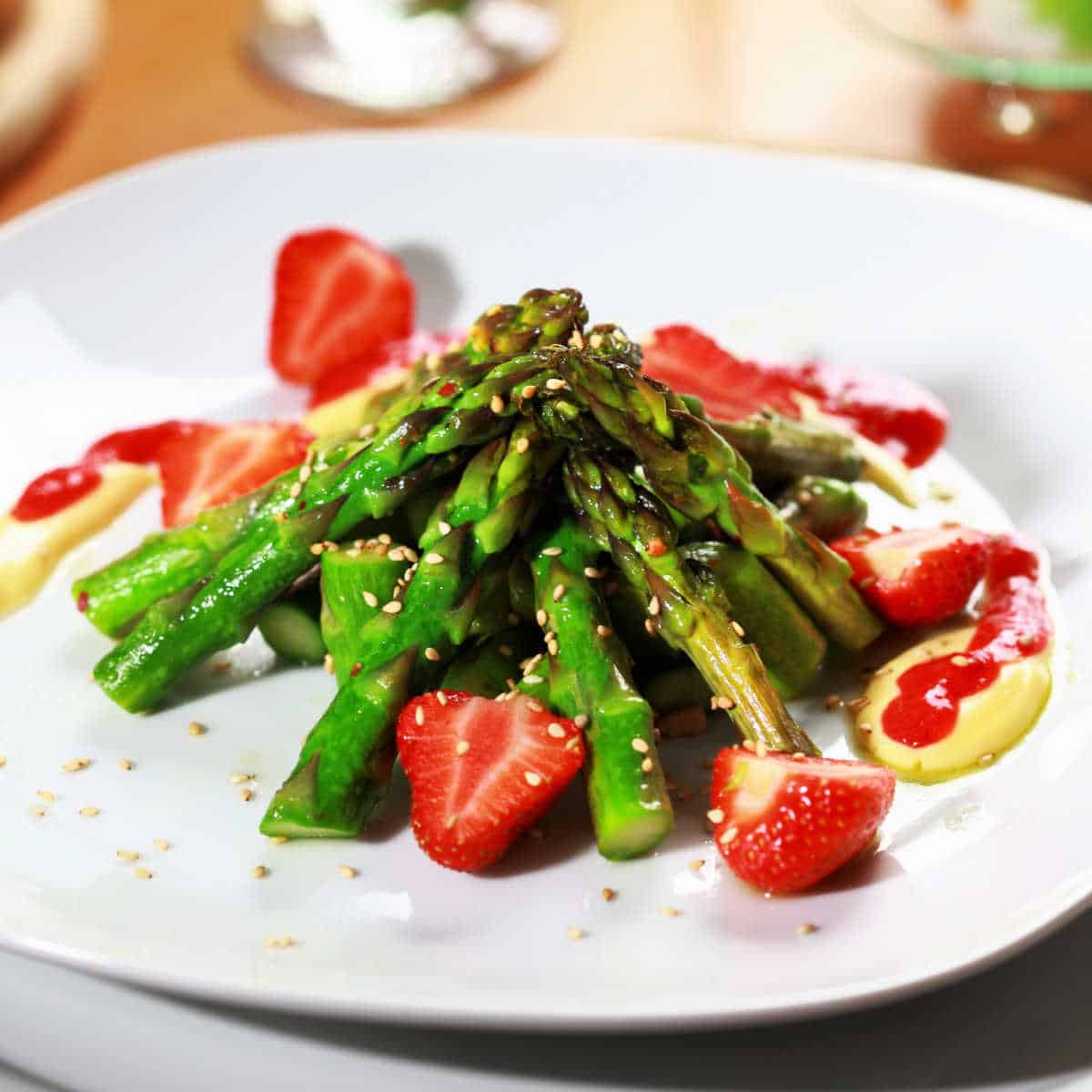 Sugared asparagus with strawberries, strawberry syrup and sesame seeds on a white plate
